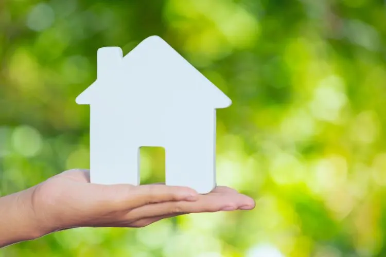 Image of house model. held in hand. Set against green background.