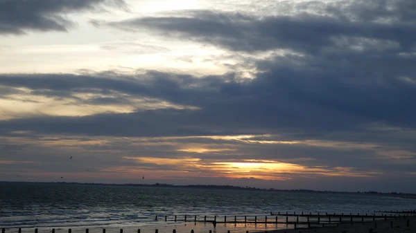 Image of seafront at dusk, with sunlight shining through clouds